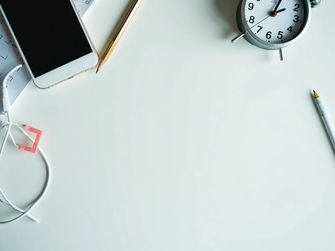 Phone face down, blank issue checklist, pencil, charging cable and clock on a clean desk